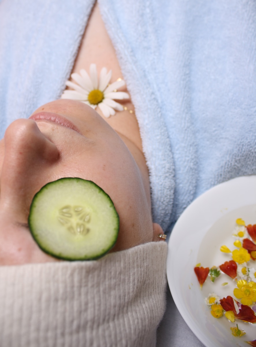 woman wearing blue robe lying with cucumber on eye