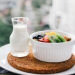 fruit salad inside bowl beside glass of milk on brown board